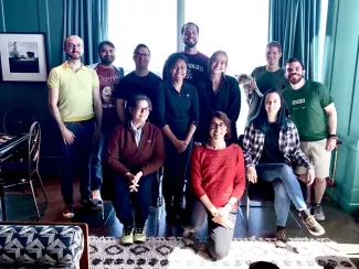 Several young people stand in a living room against a dark green wall smiling